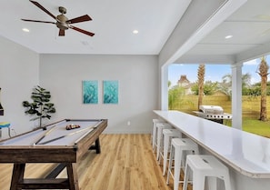 A pool table, bar stools, a ceiling fan, and a view of the backyard with a barbecue grill. - Poseidon’s Palace | 11BR | Steps 2 Beach | Heated Pool/Spa | Sleeps 28 | Games (Destin)