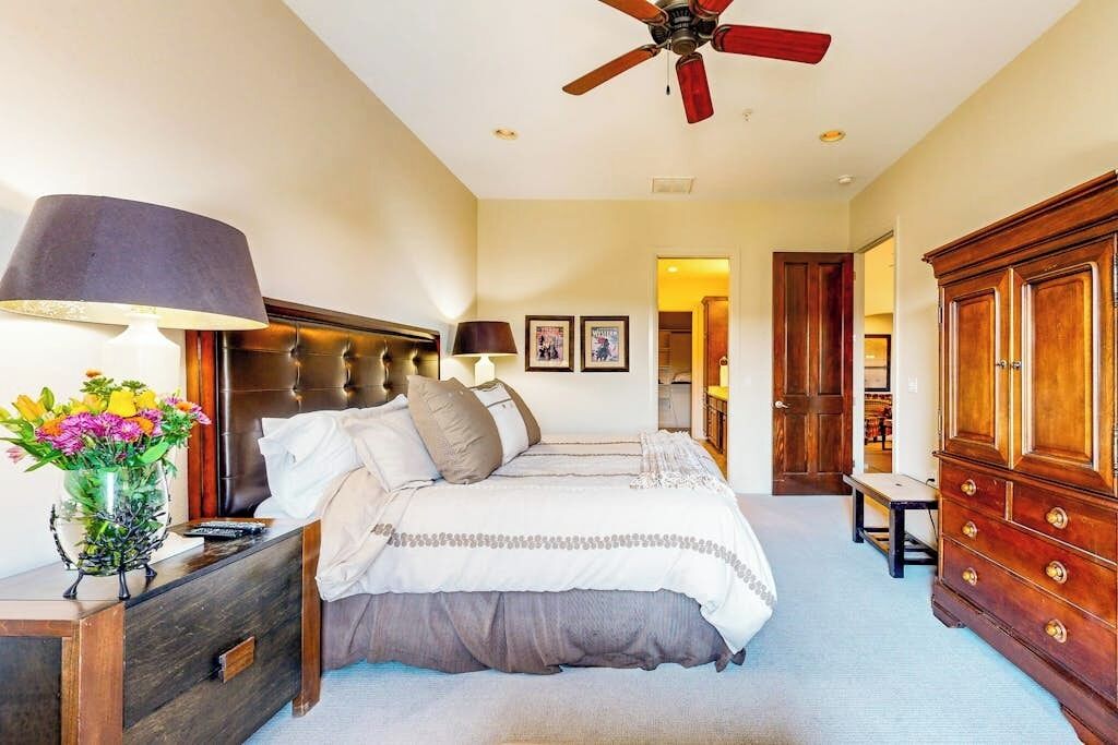 A bedroom with a bed, bedside tables, a nightstand, a dresser, a ceiling fan, and framed pictures on the wall.