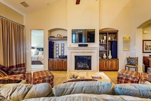 A spacious living room with a fireplace, a television mounted above it, and a seating area with patterned sofas. - Waterfront All-Suite w/ Private Balcony – On-Site Dining, Spa & Marina (Lakeway)