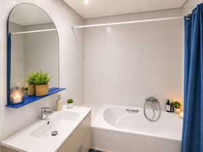 Une salle de bain équipée d’un lavabo, d’un miroir et d’une baignoire, avec des carreaux blancs et des touches de couleur bleue.