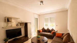 Een woonkamer met een flatscreen televisie, bank, salontafel en een kleine plant.