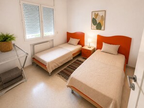 A bedroom with two single beds, a nightstand with a lamp, a radiator, a window with blinds, and a wall-mounted plant. - CosyStay Apartment (Tunis)