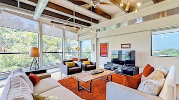 Una sala de estar moderna con un televisor grande, asientos cómodos y ventanas amplias con vistas al exterior.