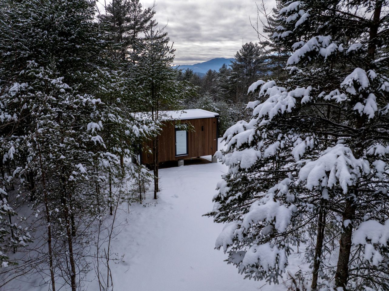 A cabin surrounded by snow-covered trees, with a clear view of the mountains in the background.