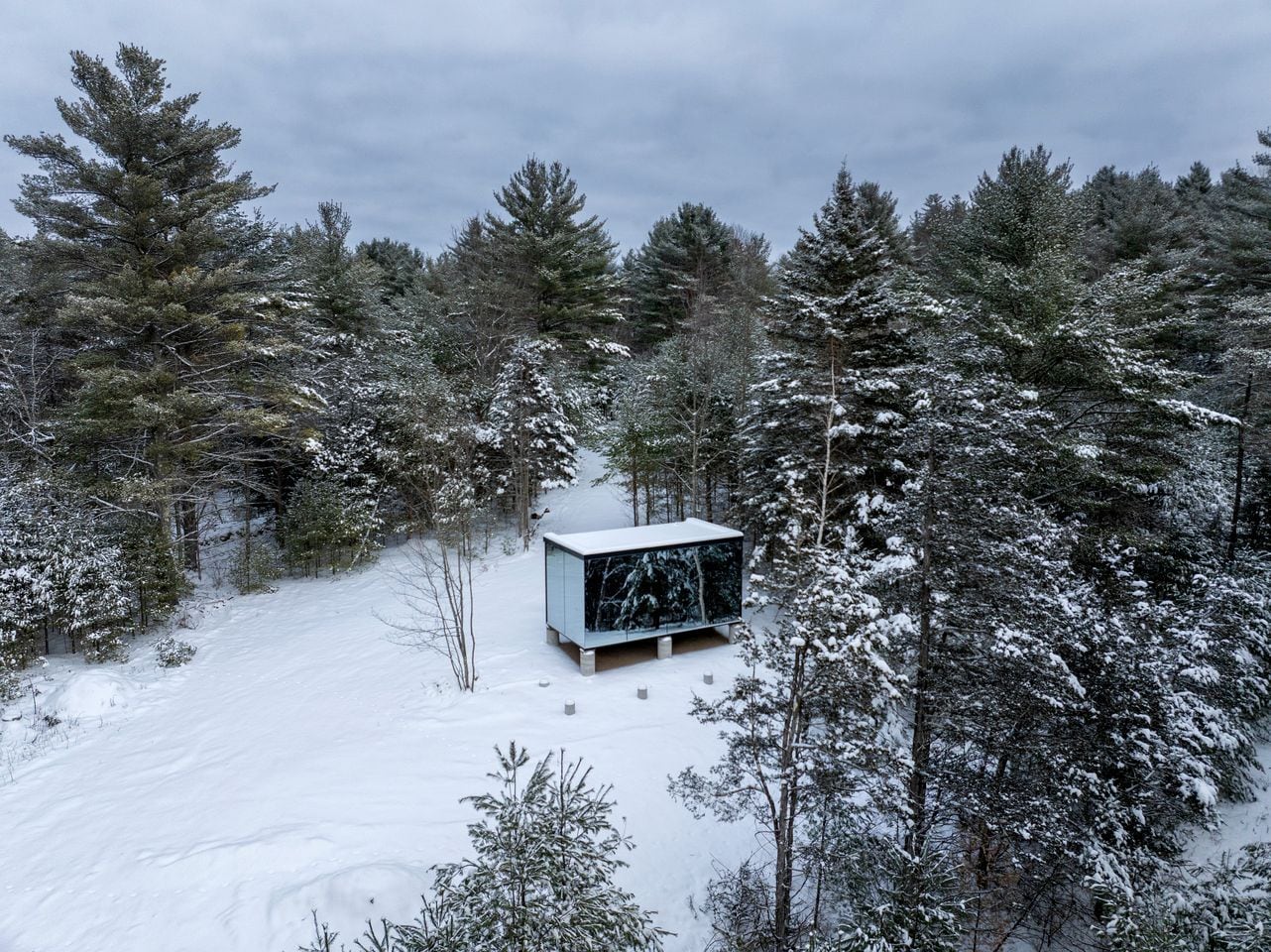 A cabin in a snowy forest with a clear view of the surrounding trees.