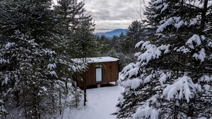 Una cabaña rodeada de árboles cubiertos de nieve, con una vista despejada de las montañas al fondo.