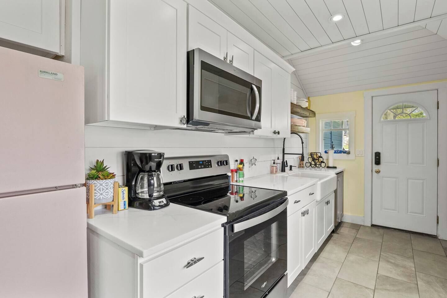 A kitchen with white cabinets, a stainless steel microwave, a coffee maker, and a refrigerator.