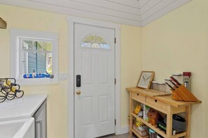 A kitchen with a white door, a window with a view, a wooden shelf with kitchenware, and a countertop with a wine rack.