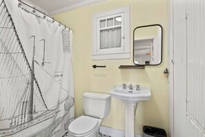 A bathroom with a toilet, sink, mirror, and a shower curtain with a nautical design.