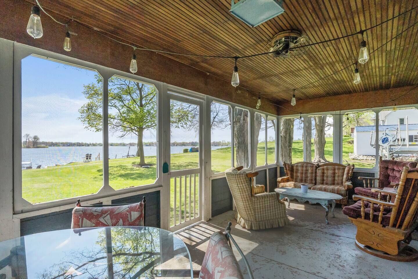 A covered porch with large windows, wooden ceiling, and rustic furniture.