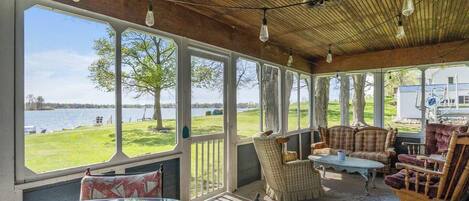 A covered porch with large windows, wooden ceiling, and rustic furniture.