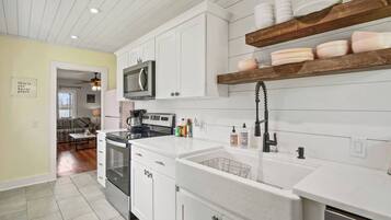 A kitchen with white cabinets, a microwave, a stove, and a sink with a faucet. There are shelves above the sink holding dishes.