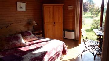 Ein Schlafzimmer einer Holzhütte mit Bett, Kleiderschrank, Tisch und Blick ins Freie.