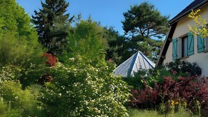 Une maison avec un toit en pente, entourée d’une végétation luxuriante et d’arbres.
