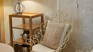 Une pièce comprenant une chaise à armature métallique, une table d’appoint en bois avec une lampe, et un mur décoré de guirlandes lumineuses en forme de cœur.