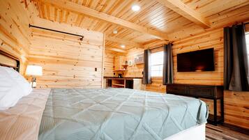 Ein Zimmer in einer Holzhütte mit einem Bett, einem Fernseher, einem Schreibtisch und einem Fenster.