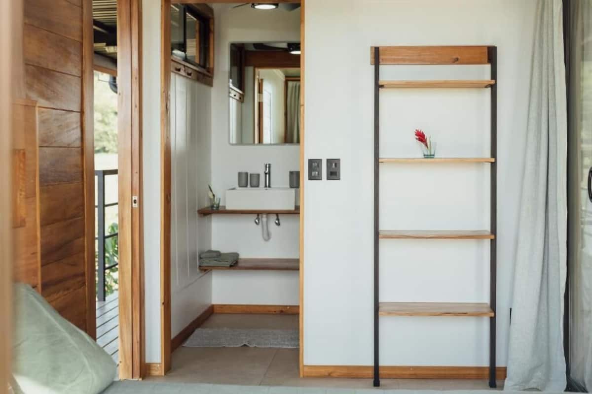 Un pasillo estrecho con una puerta de madera, un lavamanos pequeño con un espejo y un armario de madera.