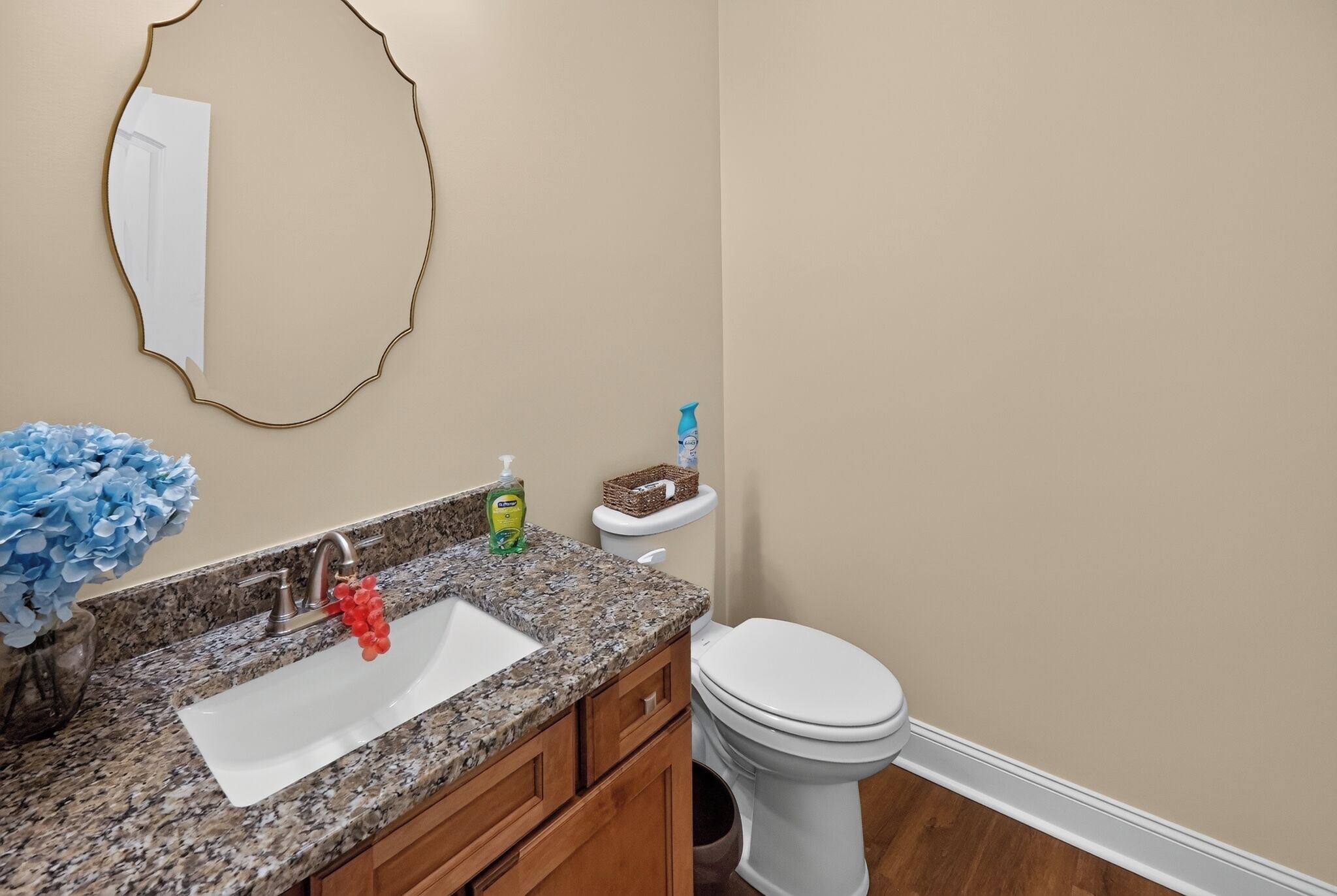 Un baño con encimera de granito, un lavabo blanco, un espejo, un inodoro y un cubo de basura.