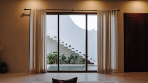 Ein modernes Interieur mit einer Couch, einer Treppe, die zu einem Balkon führt, und Blick auf ein Gebäude.