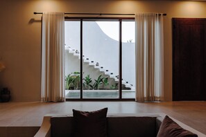 A modern interior with a sofa, a staircase leading to a balcony, and a view of a building outside. - Pleasant 2-bedroom house with AC in charming Kuta (Kuta, Central Lombok / Lombok Tengah)