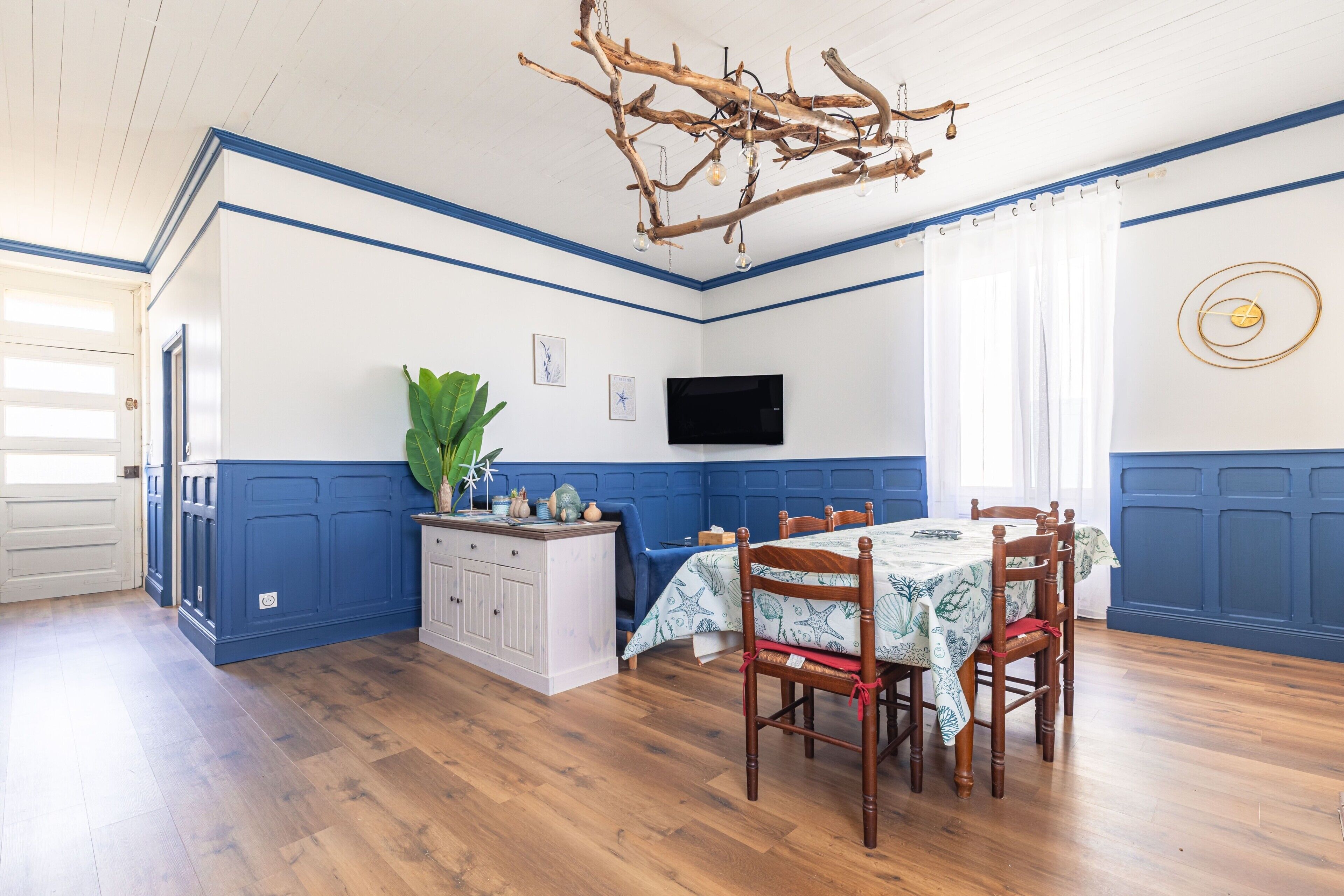 A dining area with a wooden table, chairs, a chandelier, and a television on the wall.