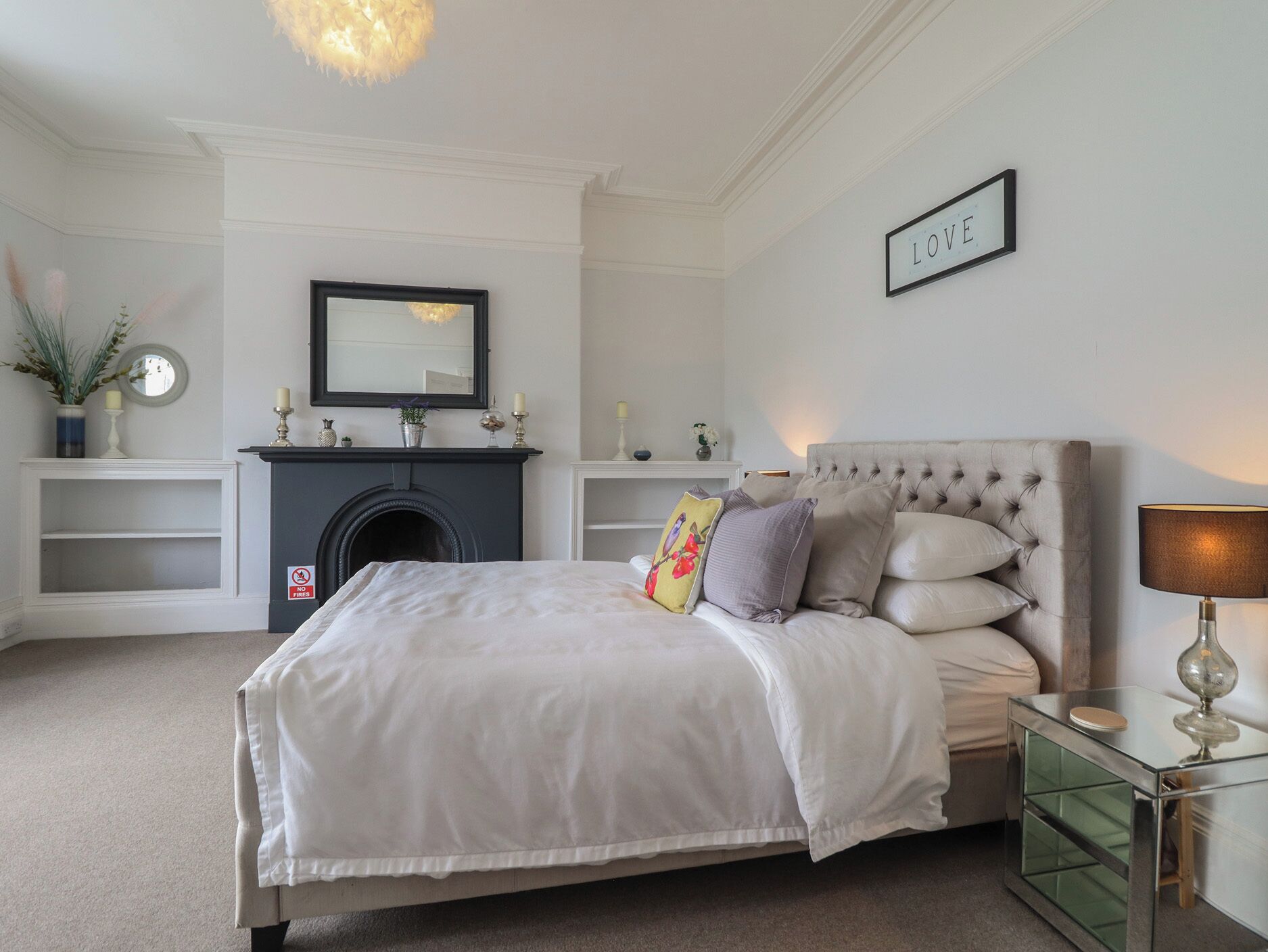 Un dormitorio con cama, chimenea, espejo y un letrero en la pared con la palabra 'LOVE'.