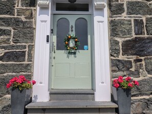 Un bâtiment en pierre avec une porte verte, deux pots de fleurs et une guirlande.