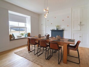 Un coin repas comprenant une table en bois, six chaises, un lustre, une cheminée et une fenêtre donnant sur un paysage.