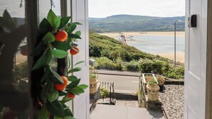 A view from a doorway to a coastal landscape with a beach, railway tracks, and greenery. - 5 Porkington Terrace (Barmouth)
