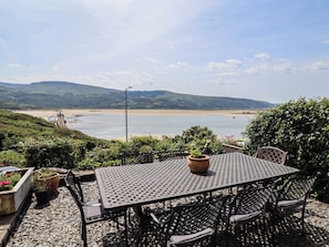 Ein Tisch und Stühle auf einer Terrasse mit Blick auf einen Strand und Hügeln in der Ferne.
