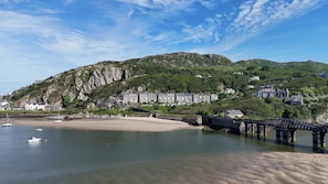 A coastal town with a beach, a stone bridge, and buildings on a hillside. - 5 Porkington Terrace (Barmouth)