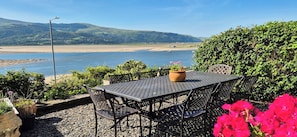 Ein Außenbereich mit Tisch und Stühlen, einem Blumentopf und Blick auf Strand und Hügel.