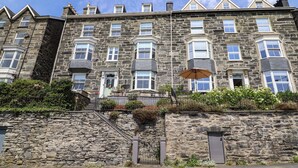 A multi-story stone building with a traditional architectural style, featuring a central entrance with a door and windows on each floor. - 5 Porkington Terrace (Barmouth)
