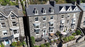 Un edificio de varios pisos de piedra con un balcón, un pequeño jardín y una escalera que lleva a la entrada.