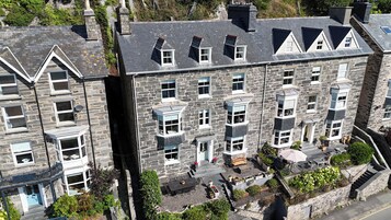 A multi-story stone building with a balcony, a small garden area, and a staircase leading to the entrance.