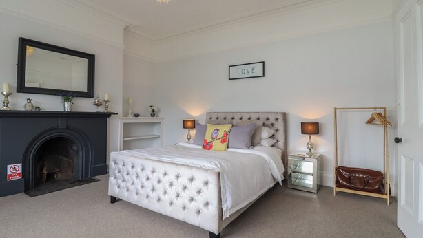 A bedroom with a bed, a fireplace, a mirror, a 'LOVE' sign, and a coat rack. - 5 Porkington Terrace (Barmouth)