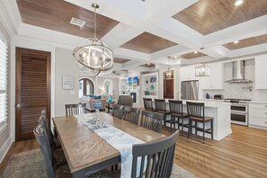 A modern kitchen with white cabinetry, a central island, and a dining area with a wooden table and chairs. - Bikes, Gated Community, New Rental, Golf Cart, Hot Tub, Close to Beach (Santa Rosa Beach)