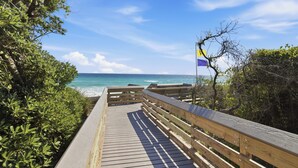 A wooden boardwalk leading to a beach with a flag, surrounded by greenery. - Bikes, Gated Community, New Rental, Golf Cart, Hot Tub, Close to Beach (Santa Rosa Beach)