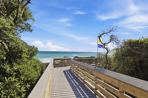A wooden boardwalk leading to a beach with a flag, surrounded by greenery. - Bikes, Gated Community, New Rental, Golf Cart, Hot Tub, Close to Beach (Santa Rosa Beach)