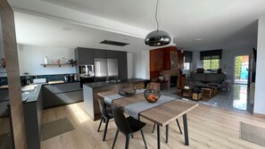 Eine moderne Küche mit Kochinsel, Essbereich mit Tisch und Stühlen sowie ein Wohnzimmer mit Sofa und Fernseher.
