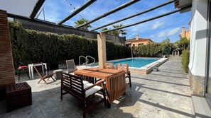 Ein Poolbereich mit Holztisch und Stühlen, einer Pergola und einem Schwimmbecken.