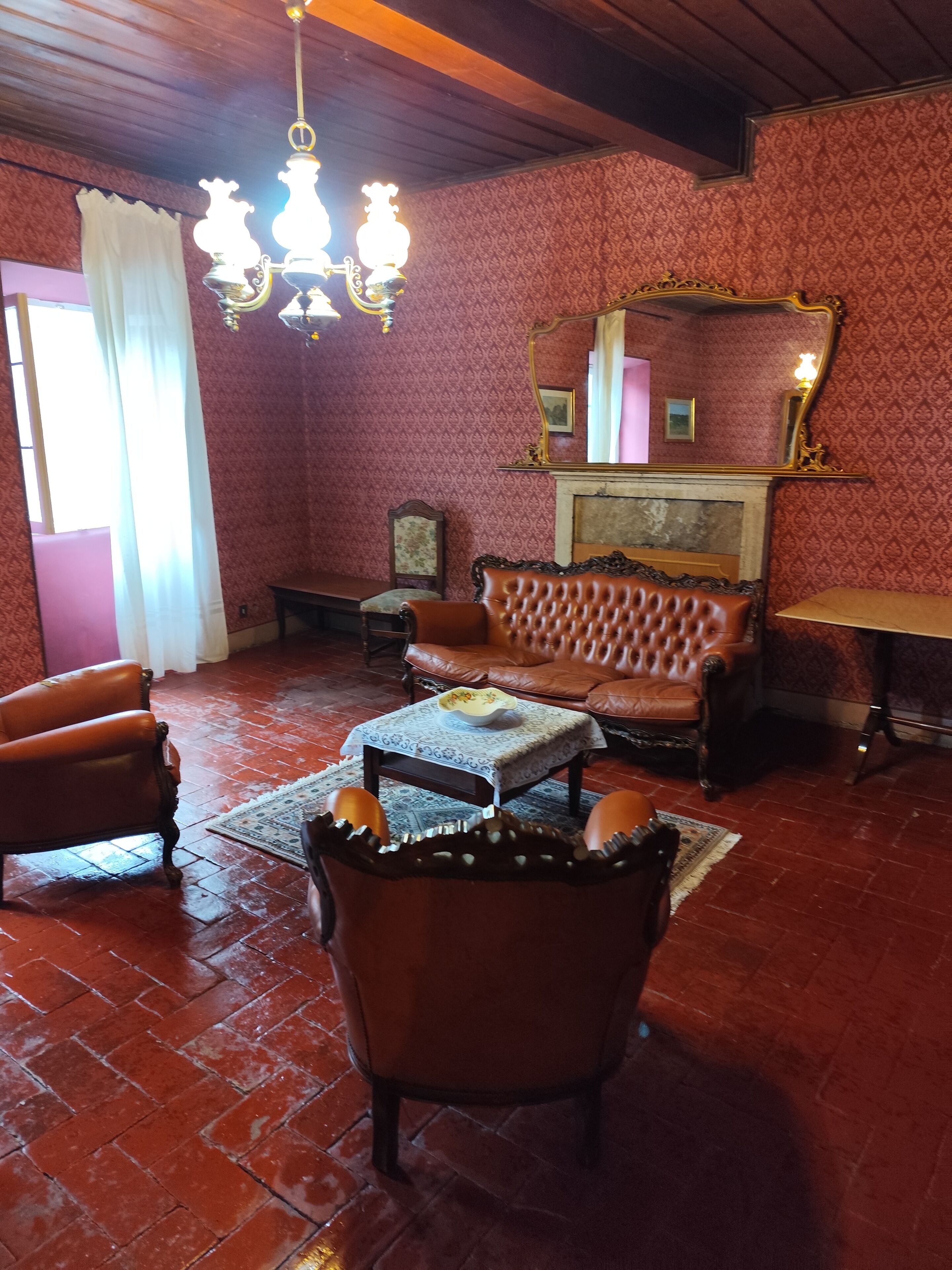 Une pièce avec un papier peint à motifs, un lustre, une cheminée, un canapé et une table sur laquelle se trouve un bol.