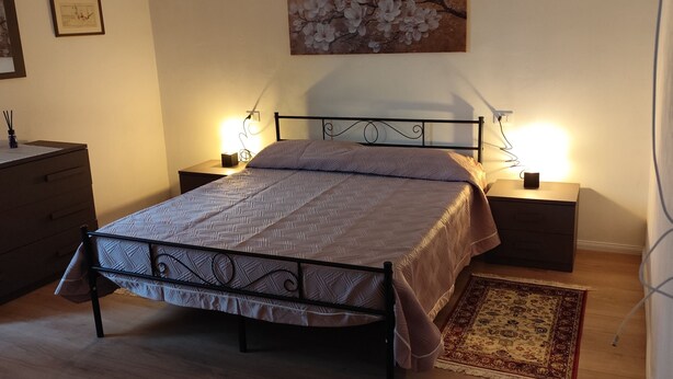 A bedroom with a bed, bedside tables, a nightstand, a dresser, a painting, and a rug.