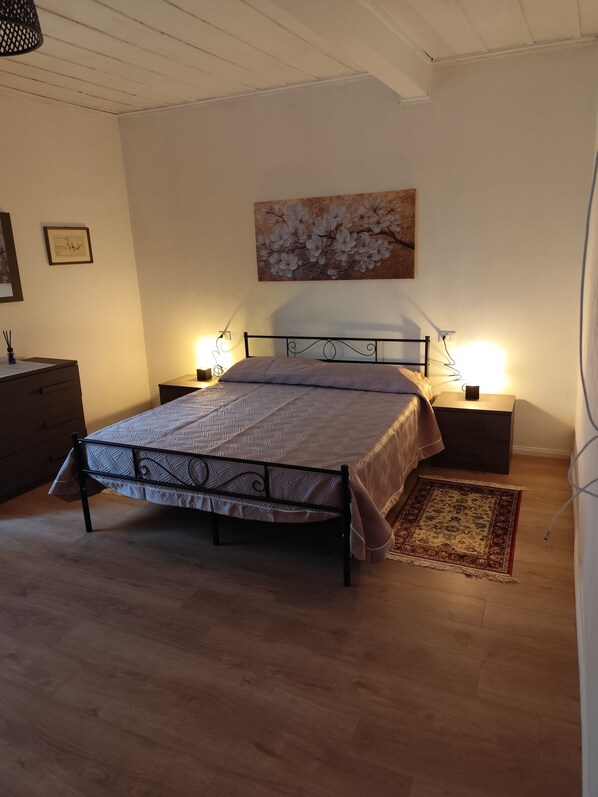 A bedroom with a bed, bedside tables, a nightstand, a dresser, a painting, and a rug.