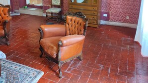 A room with a patterned wallpaper, a wooden cabinet, a leather armchair, and a tiled floor.
