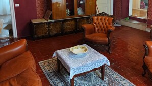 A room with a patterned wallpaper, a wooden cabinet, a leather armchair, a table with a white tablecloth, and a patterned rug.