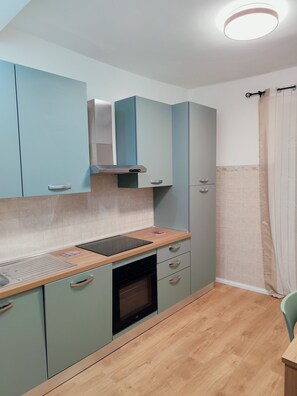 Une cuisine compacte avec des meubles de couleur bleu clair, un plan de travail en bois, un four encastré et un luminaire au plafond.