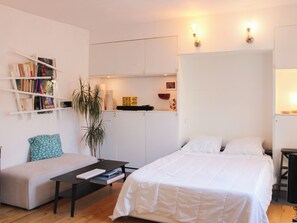 A compact room with a bed, a sofa, a small table, a bookshelf, and a kitchen area. - Charming studio with courtyard near Père-Lachaise (Paris)