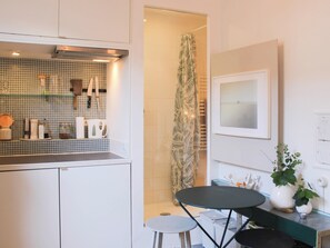 A compact kitchen with a tiled backsplash, a small dining area with stools, and a shower with a leaf-patterned curtain. - Charming studio with courtyard near Père-Lachaise (Paris)