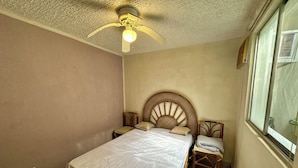 Ein Schlafzimmer mit Bett, Deckenventilator, Fenster und Nachttisch.